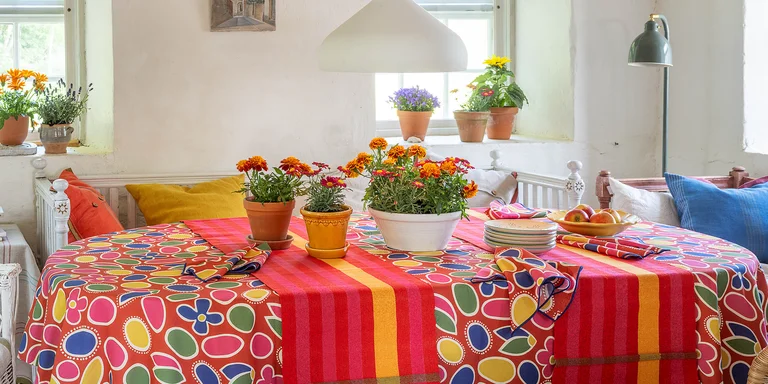 A round table with a colorful patterned tablecloth and napkins in shades of red and a striped table runner from Gudrun Sjödén.