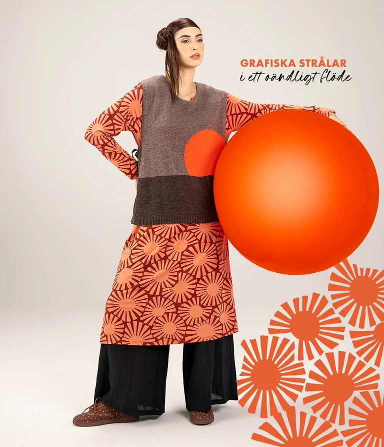 A woman standing with a large red ball, wearing layers of clothing from Gudrun Sjödén’s spring extra collection 2026.