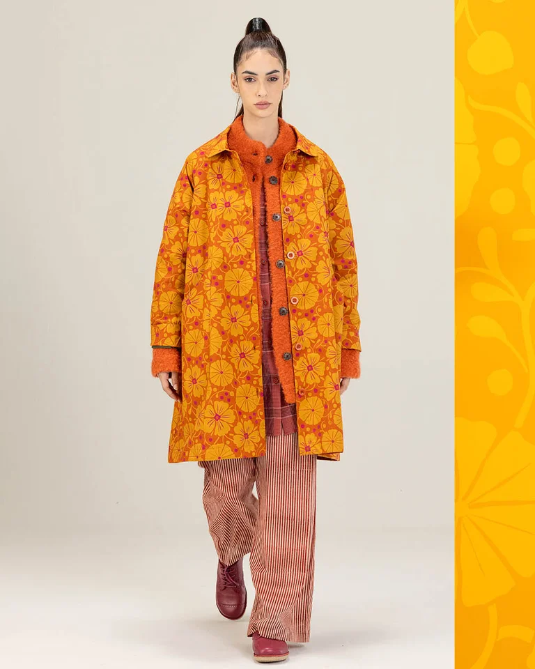 A woman photographed from the front wearing a patterned orange coat from Gudrun Sjödén.