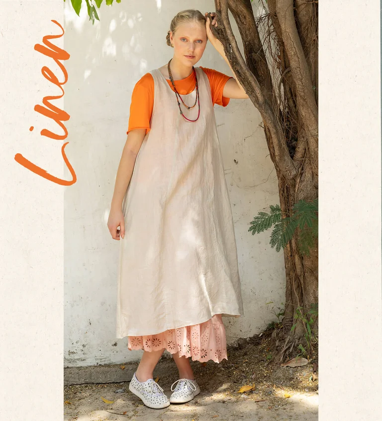 En kvinna klädd i orange topp och naturfärgad klänning från Gudrun Sjödén.  