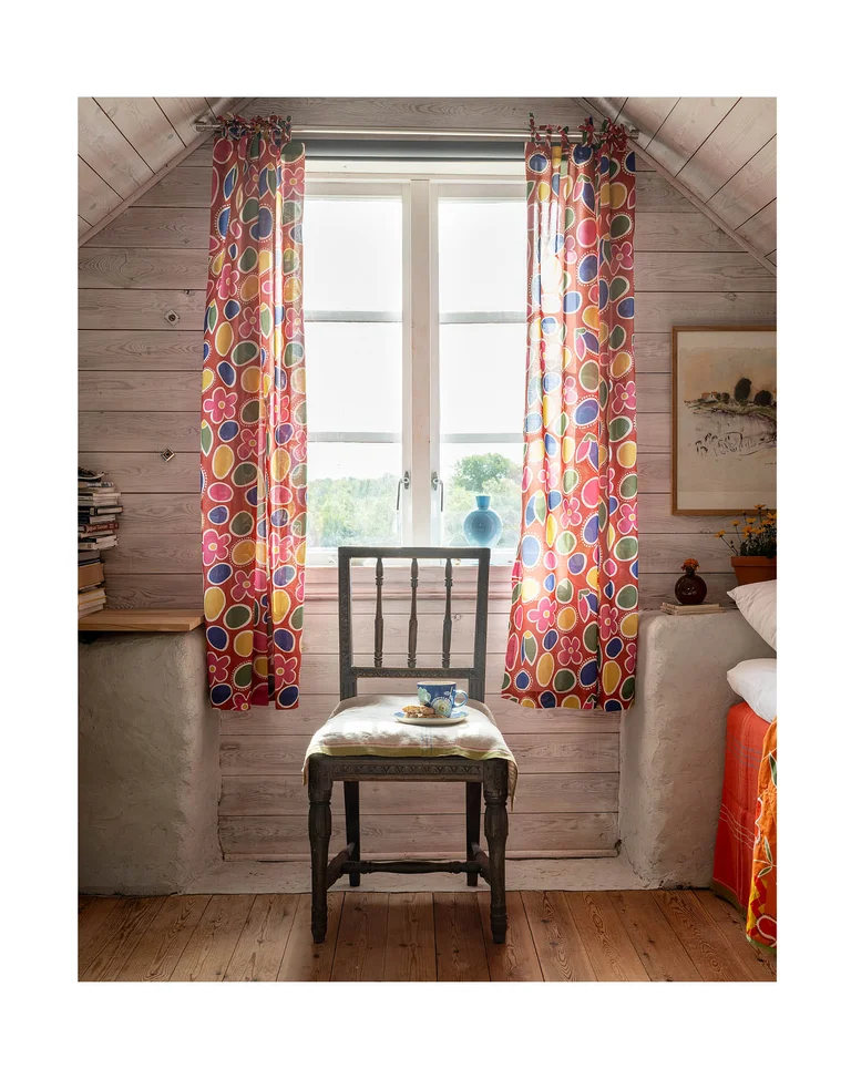A chair under an attic window with patterned curtains from Gudrun Sjödén.