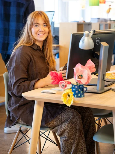 A smiling woman sitting at a desk at Gudrun Sjödén's headquarters.