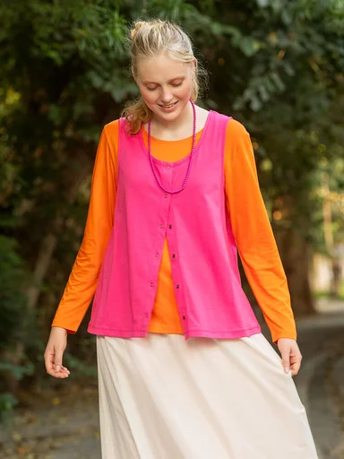A woman wearing an orange sweater and pink vest from Gudrun Sjödén. 