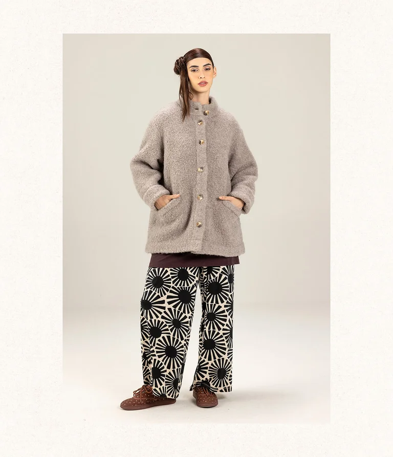 A woman wearing a beige bouclé jacket and a pair of black and white patterned pants from Gudrun Sjödén. 