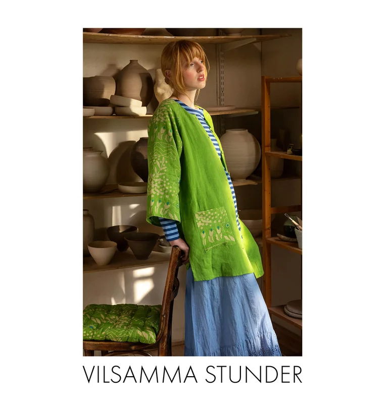 A woman in a pottery studio wearing a green “Nemorosa” linen tunic, a striped top and a light-blue skirt from Gudrun Sjödén.
