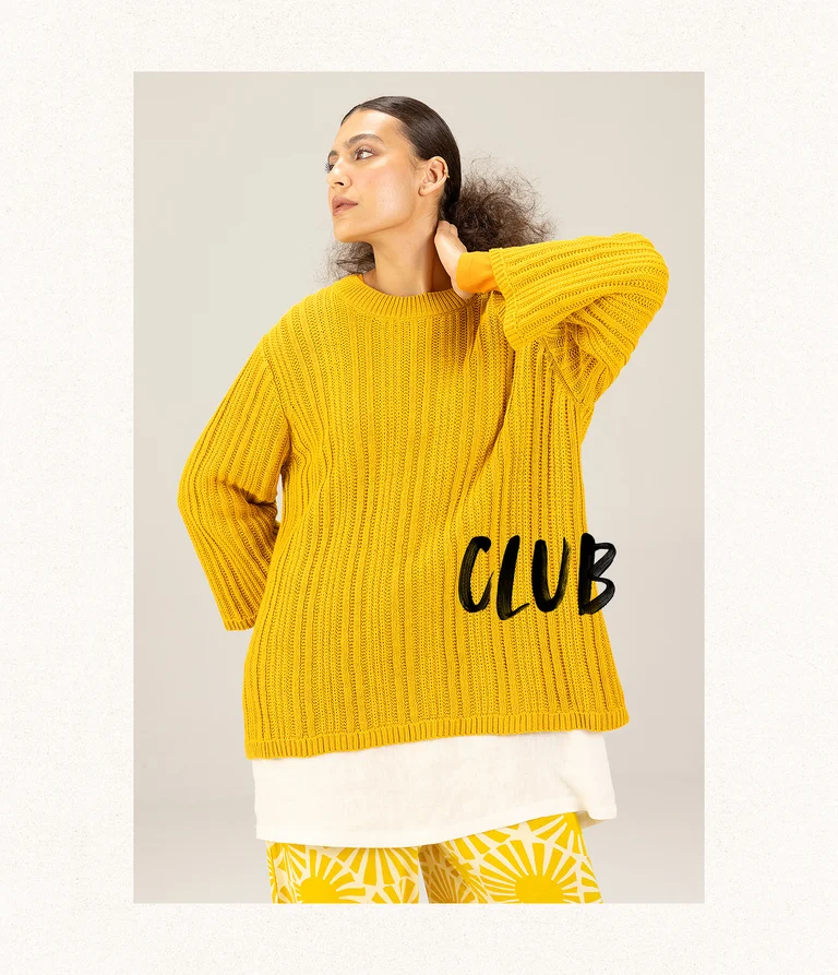 A woman posing in a yellow knit sweater from Gudrun Sjödén. 