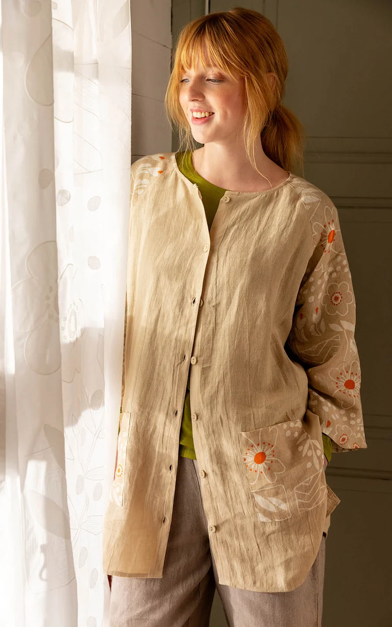 A woman in the “Nemorosa” linen tunic from Gudrun Sjödén by a sheer, white curtain from Gudrun Sjödén.