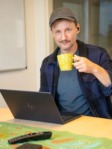 A man sitting in front of a laptop with a coffee cup in his hand at Gudrun Sjödén's headquarters.