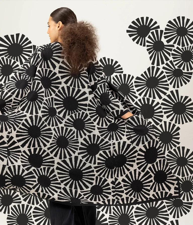 A woman with her back to the camera wearing a patterned cardigan, where the pattern appears to be flowing out over the background. 