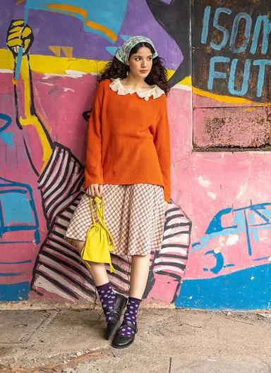 A woman leaning against a graffiti painted wall wearing layers of clothes from Gudrun Sjödén.